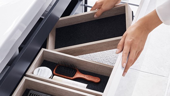 A hand opens one of the drawers of the Geberit Renova Plan washbasin cabinet in a natural wood design